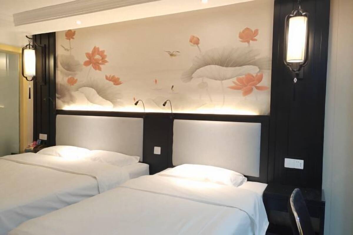 A hotel room with two beds, a large wall mural with floral and bird designs, and two wall-mounted lamps.