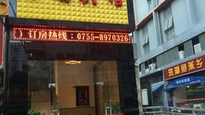 Een hotelentree met een glazen deur, een digitaal displaybord met een telefoonnummer, en een bord voor een restaurant.