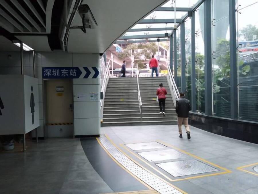 A subway station with stairs leading to an exit, a directional sign, and a glass wall.