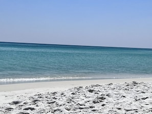 En strand med klart, blåt vand og hvidt sand.