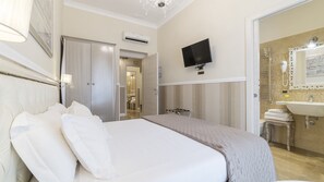 A hotel room with a large bed, a television mounted on the wall, a bathroom with a sink and mirror, and an air conditioning unit. - Elegant Apartment in the Heart of Prati with Comfortable Rooms (Roma)