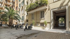 A building with a ground-floor entrance, a palm tree, and parked scooters. - Elegant Apartment in the Heart of Prati with Comfortable Rooms (Roma)
