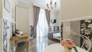 A hotel room with a bed, a TV, a desk with a chair, and a dining table with a flower vase. - Elegant Apartment in the Heart of Prati with Comfortable Rooms (Roma)