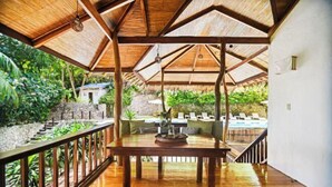 Eine Holzterrasse mit Tisch und Stühlen, umgeben von üppiger Vegetation und einem Pool.