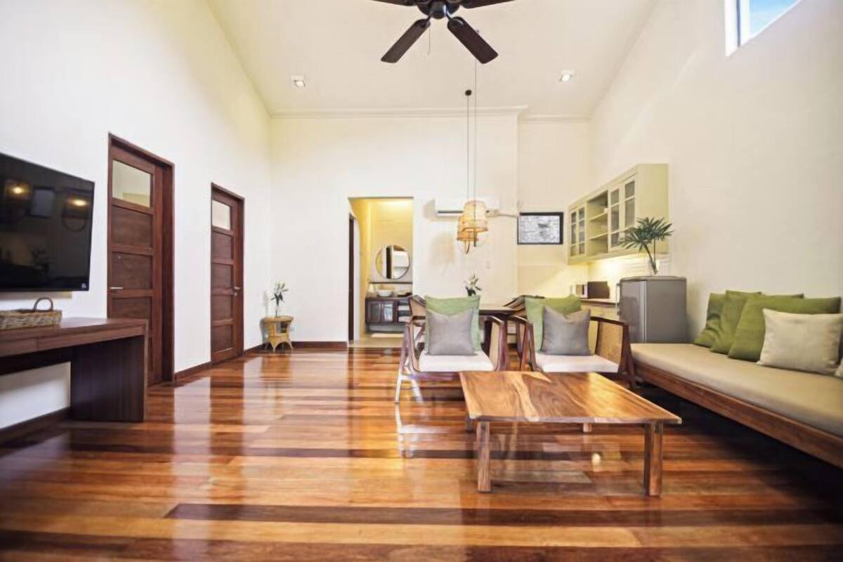 Uma sala de estar ampla com piso de madeira, ventilador de teto, sofá, mesa de centro e televisão.