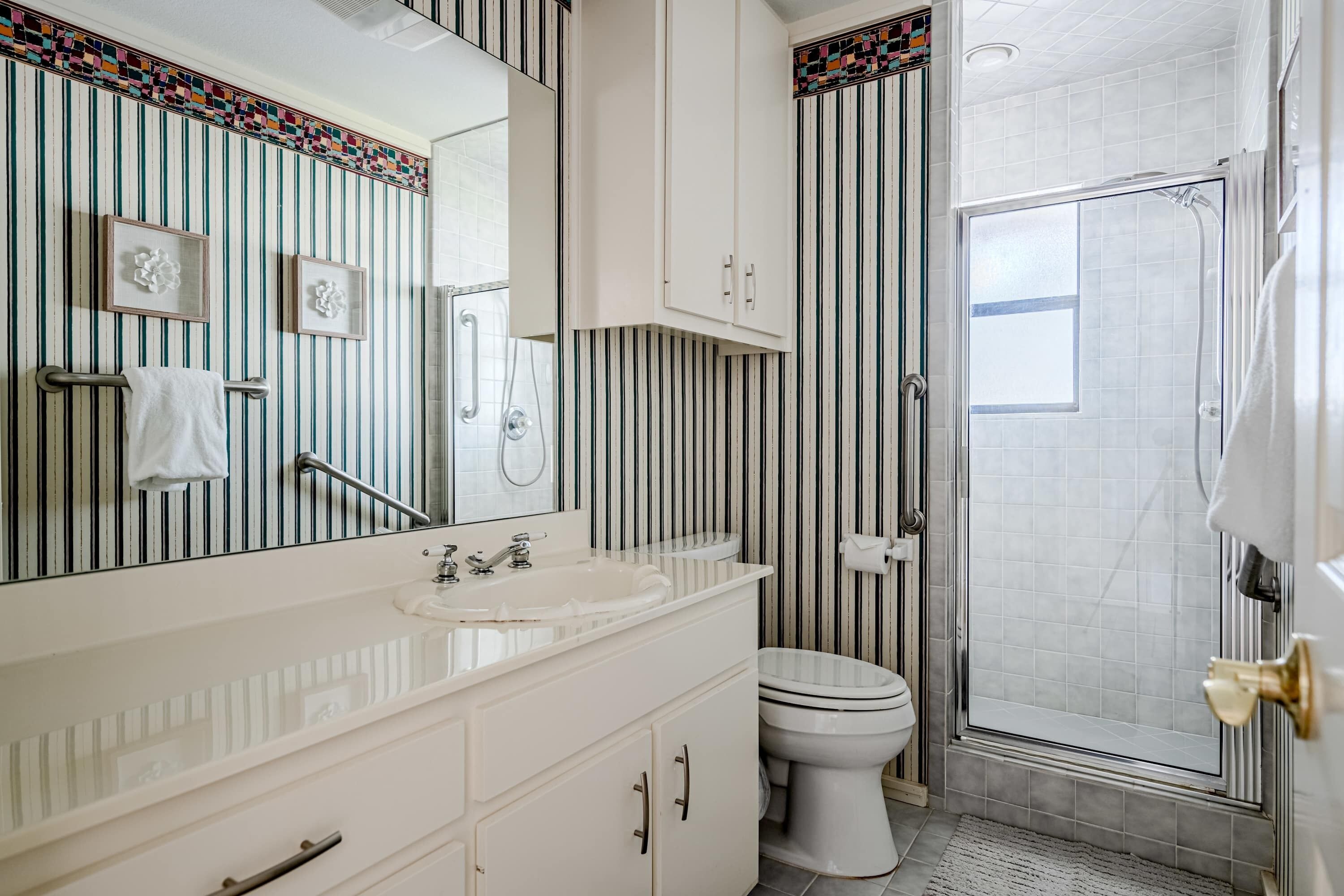 Un baño con pared a rayas, un lavamanos, un inodoro y una ducha.