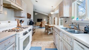 A kitchen with white cabinets, a stove, a sink, and a dining area with a chair and table. - Austin Cozy 2BR — Yard, Fire Pit, Pet OK, Sleeps 6 (Austin)