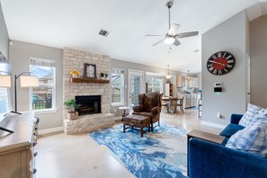 A spacious living room with a fireplace, a blue patterned rug, a blue sofa, and a dining area in the background. - Austin Cozy 2BR — Yard, Fire Pit, Pet OK, Sleeps 6 (Austin)