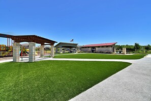 A playground with a covered area, a building with a red roof, and a well-maintained lawn. - Long-term Stays | Family-friendly | Communal pool! (Del Valle)