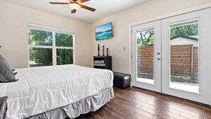 A bedroom with a bed, a ceiling fan, a TV, and a sliding glass door to the outside. - Screened-in Porch | Walkable to SoCO (Austin)