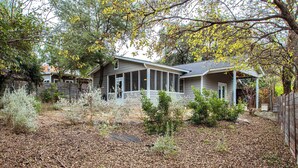A residential house with a porch, surrounded by trees and a leaf-covered yard. - Screened-in Porch | Walkable to SoCO (Austin)