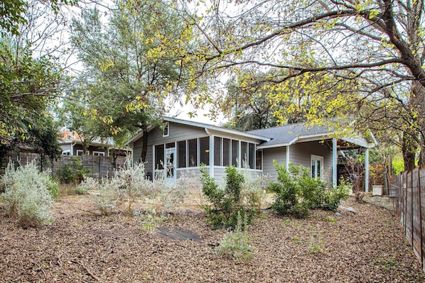 A residential house with a porch, surrounded by trees and a leaf-covered yard.