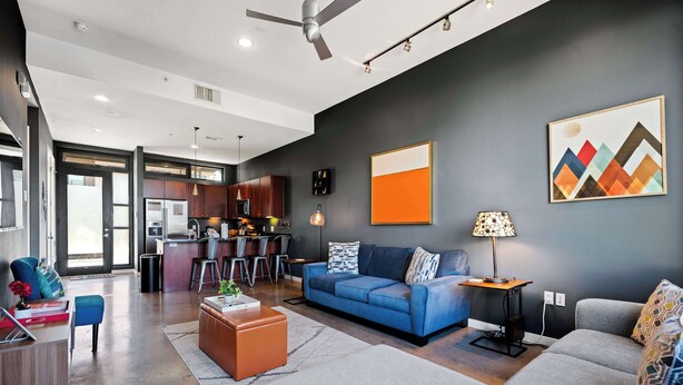 A modern living room with a sofa, coffee table, and a dining area with chairs and a kitchen in the background.