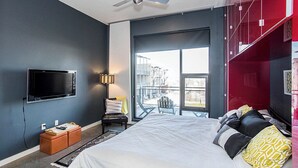 A modern bedroom with a large bed, a TV mounted on the wall, a ceiling fan, and a view of the outside through a sliding door.