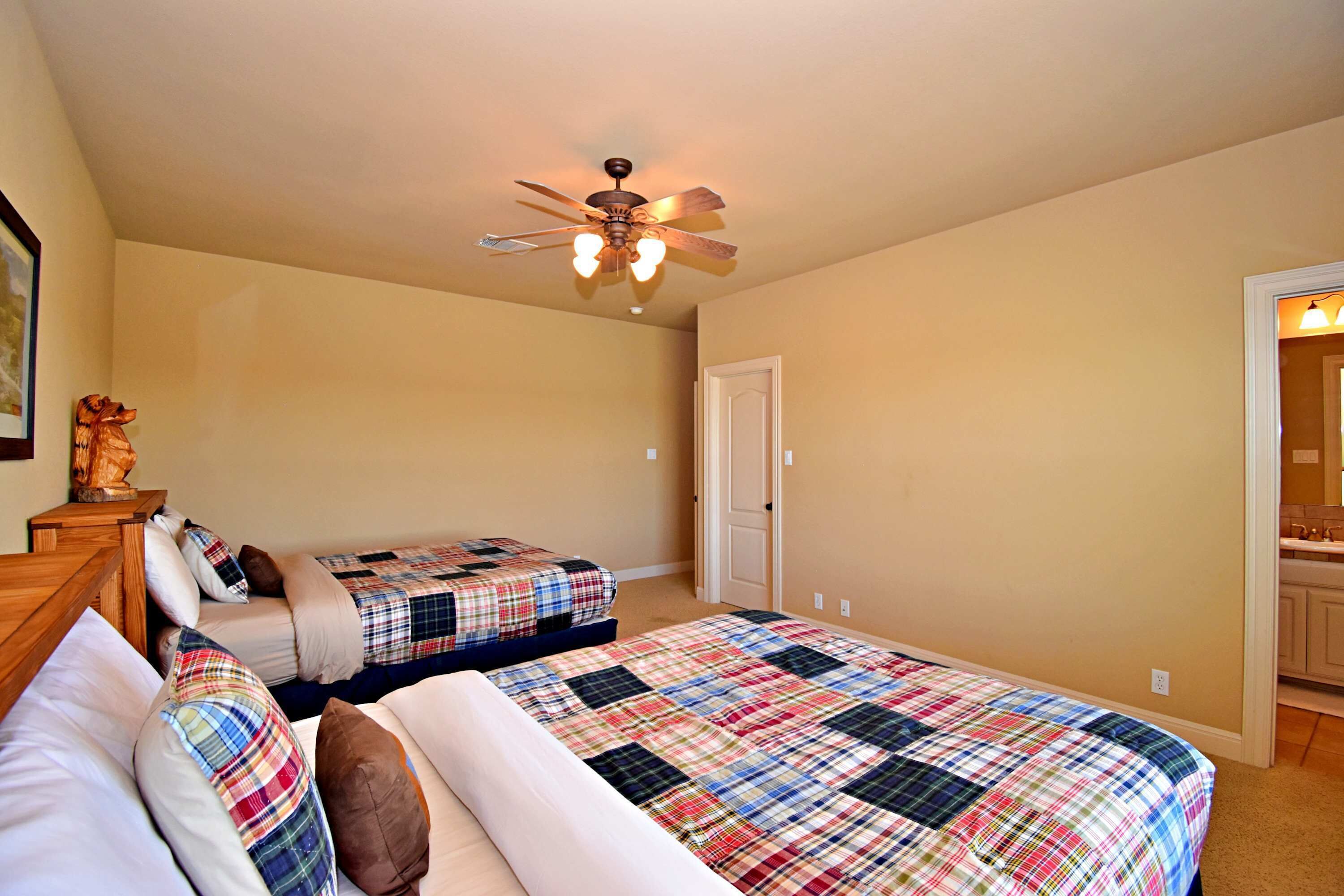 A bedroom with two beds, a ceiling fan, a door, and a small table with a statue.