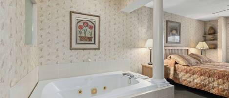 A bathroom with a large bathtub, a mirror, and a framed picture on the wall.