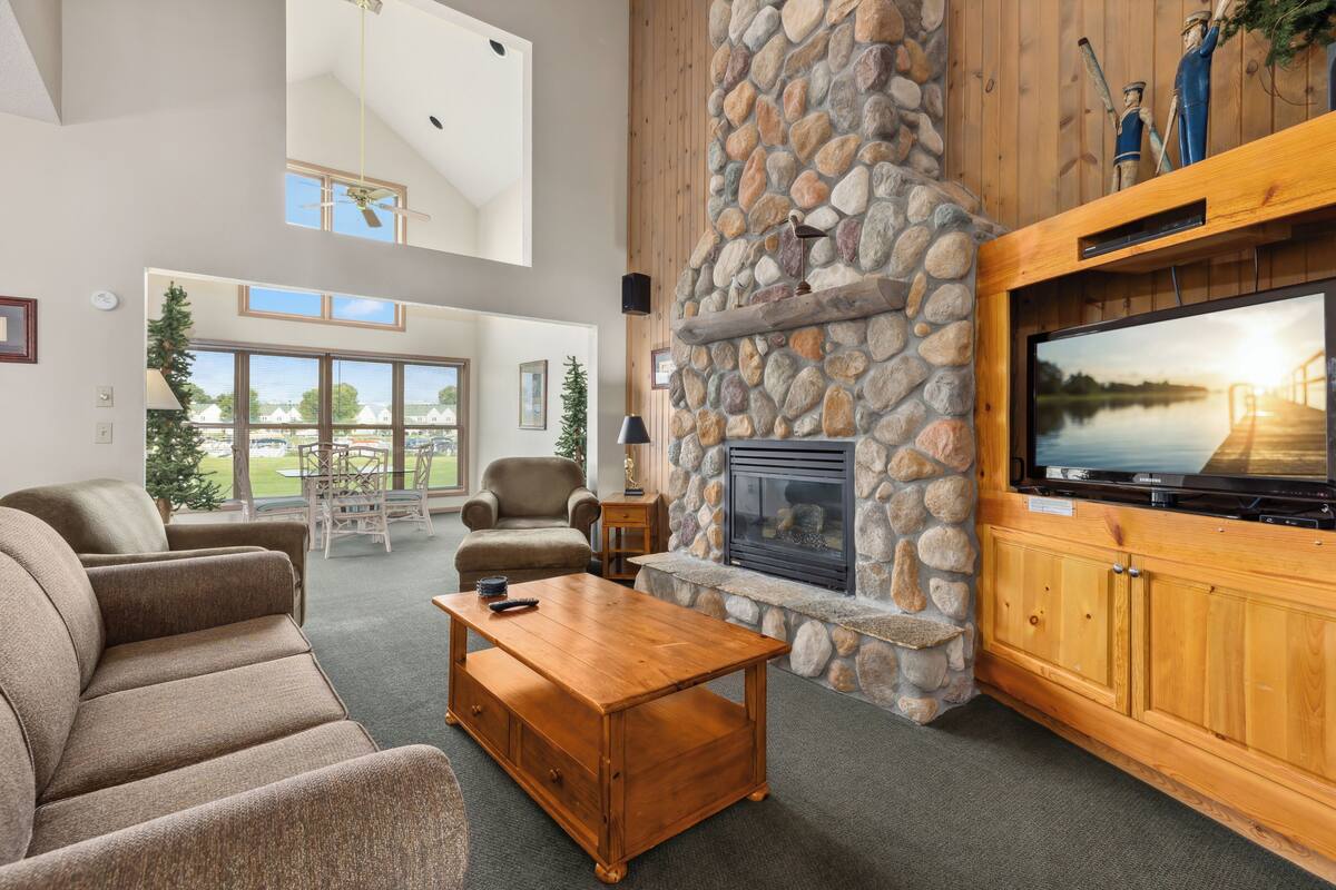 A spacious living room with a stone fireplace, a large flat-screen TV, and a cozy seating area with a coffee table.