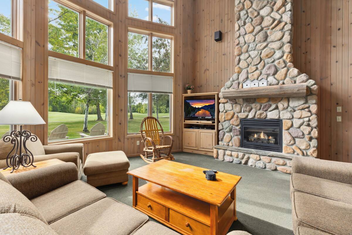 A cozy living room with a stone fireplace, large windows, and comfortable seating.