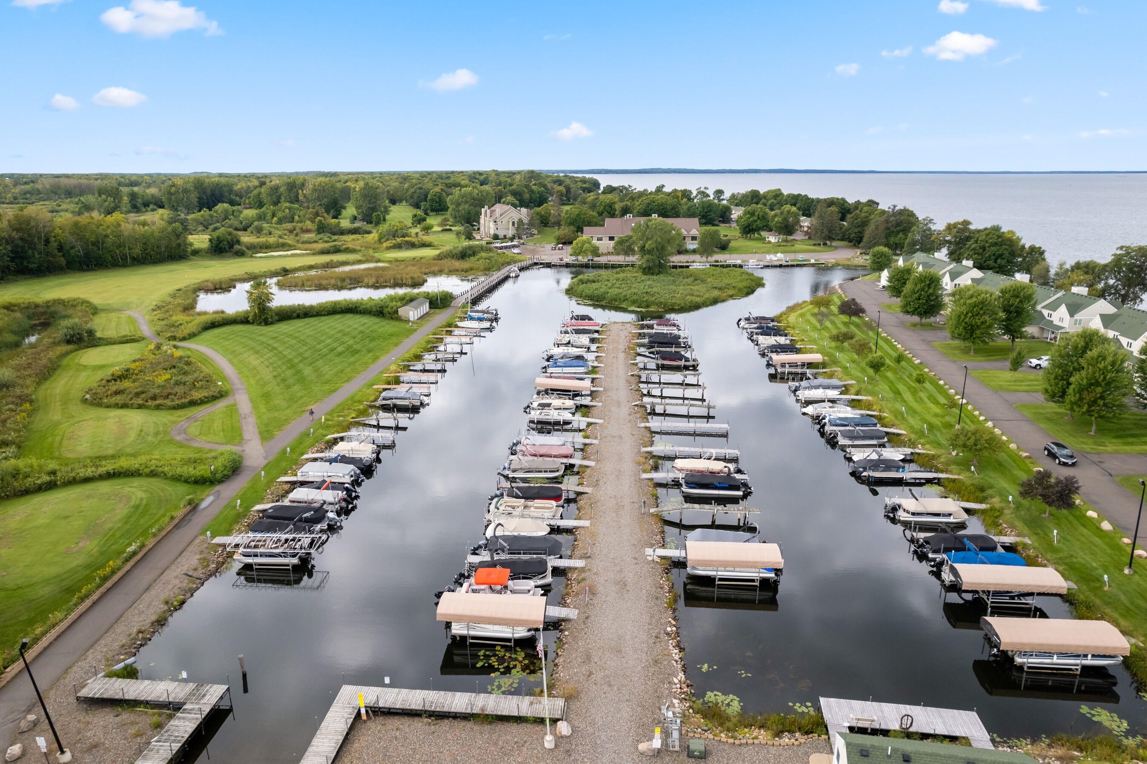 Un puerto deportivo con barcos amarrados a lo largo de un canal estrecho, rodeado de vegetación y edificios residenciales.
