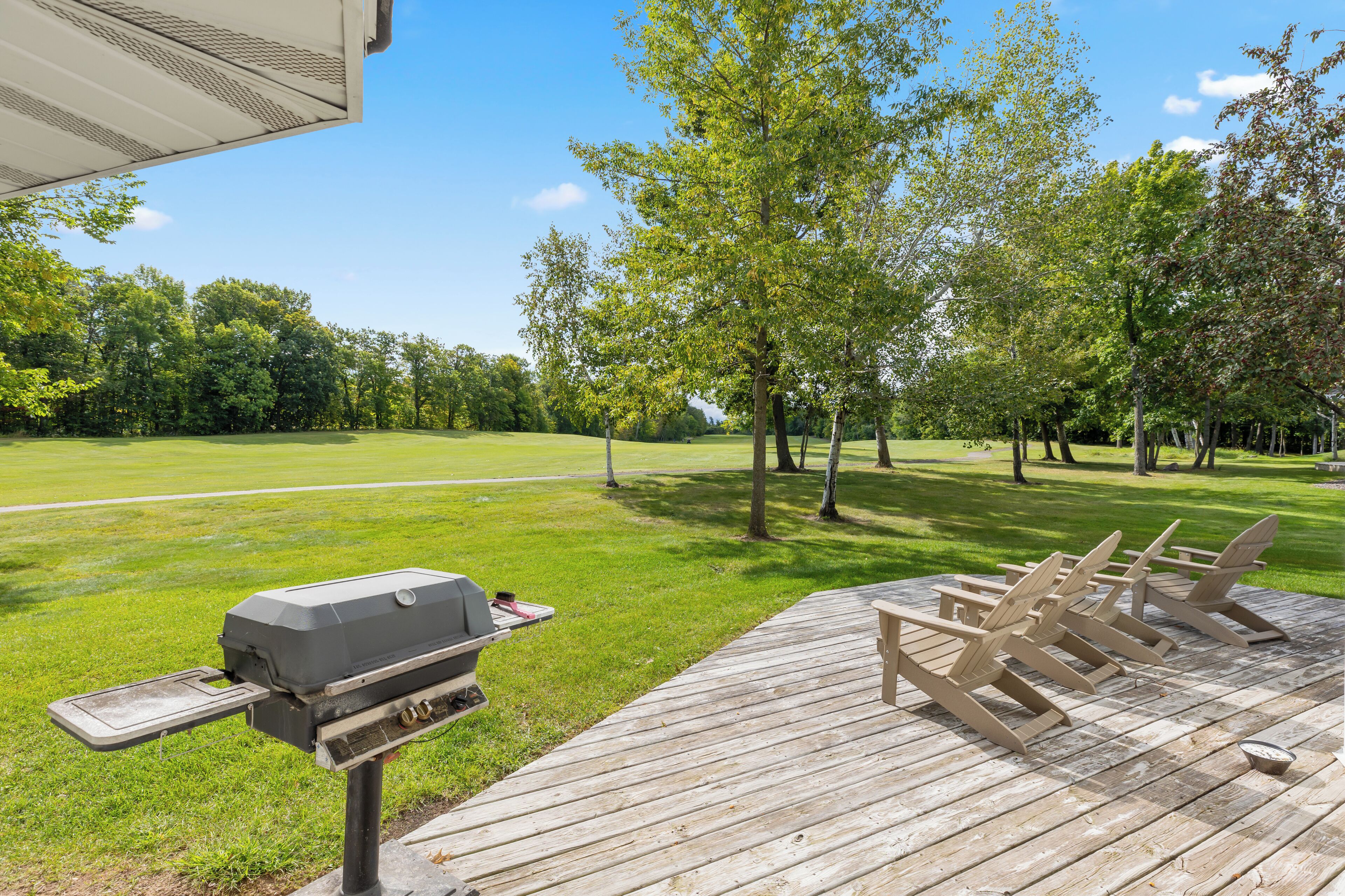 Eine Holzterrasse mit Grill und Adirondack-Stühlen.