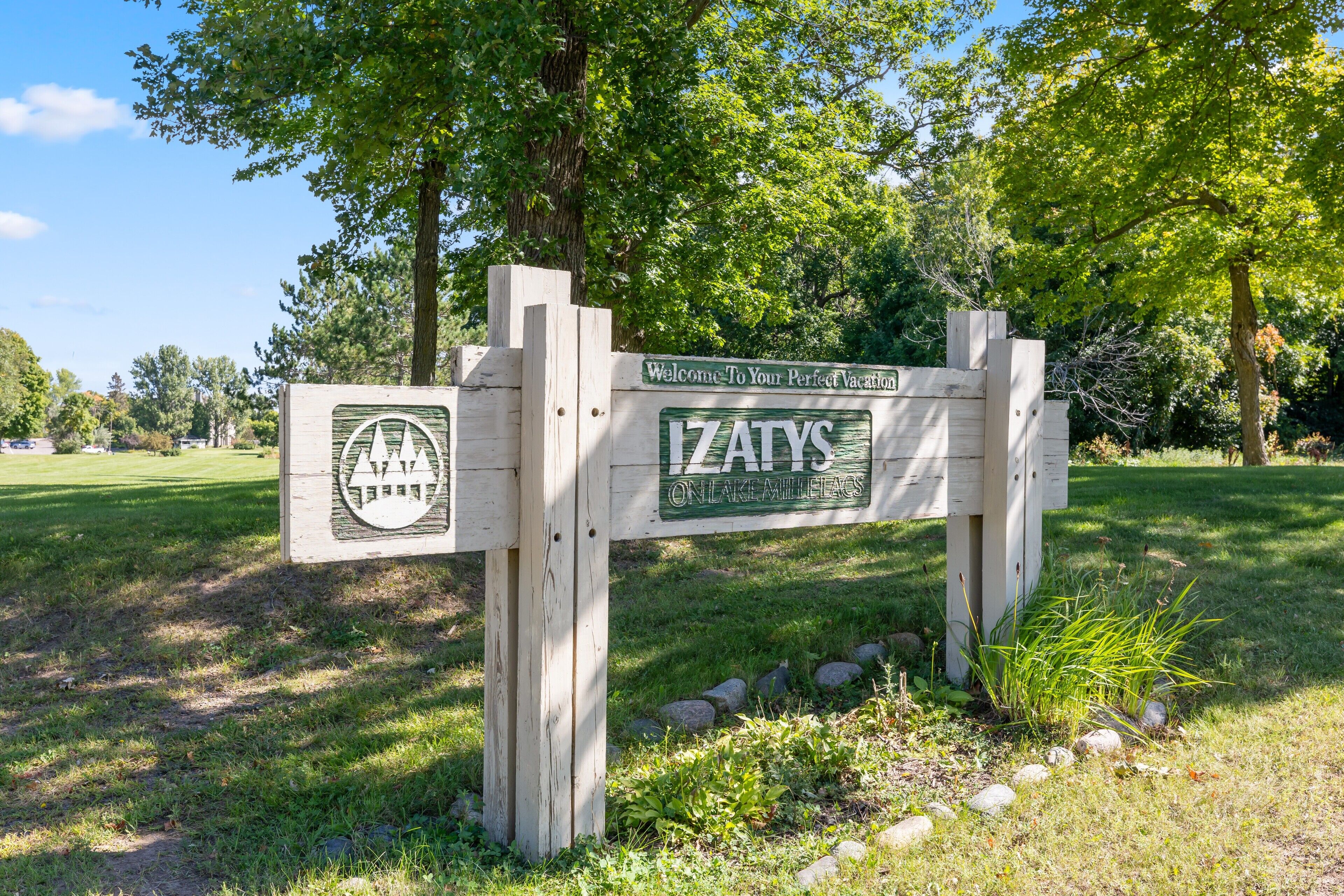 A wooden sign with the text "Welcome to Your Perfect Vacation" and "IZATYS ON LAKE MILLEGRAVES".