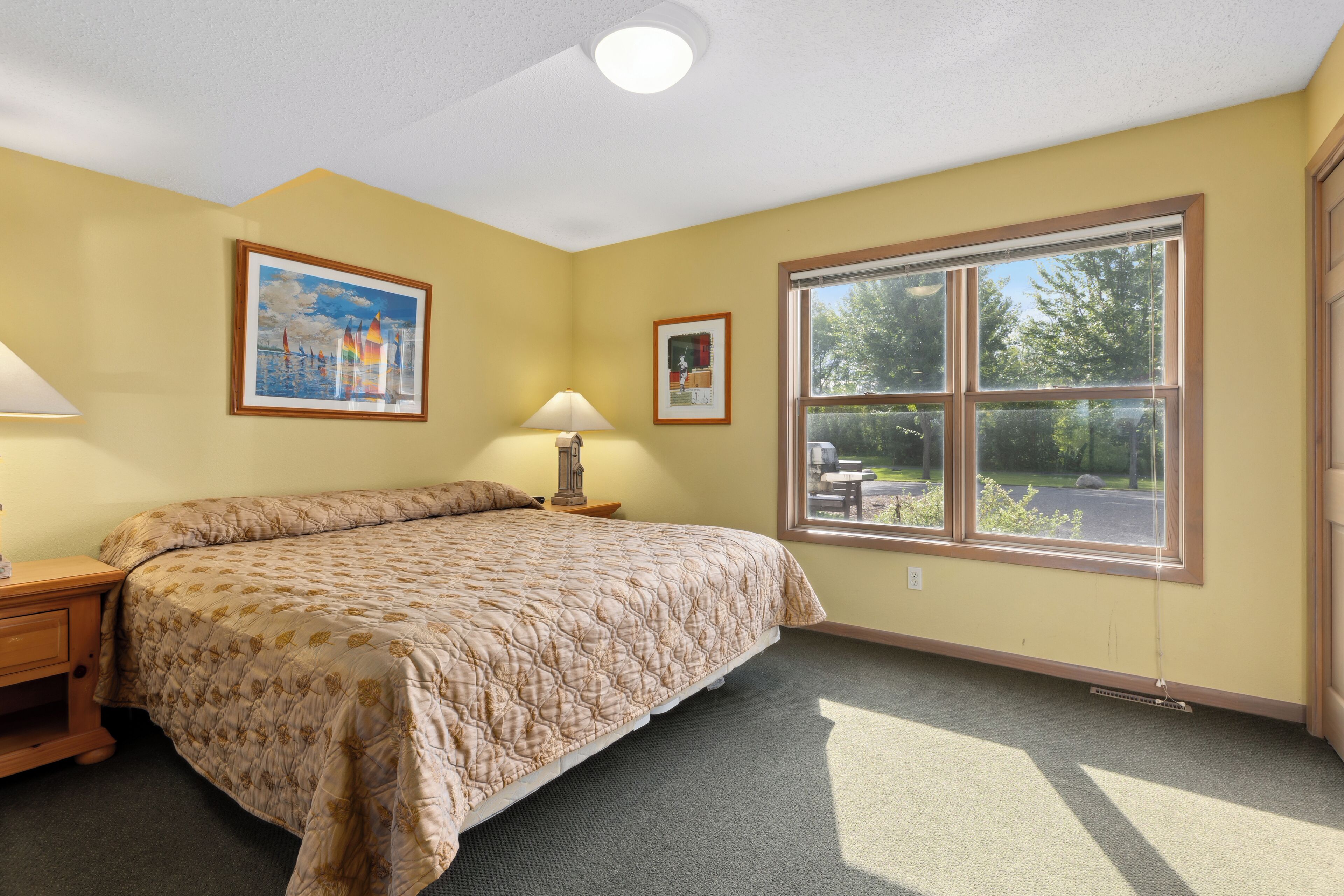 Une chambre avec un grand lit, deux tables de chevet, une fenêtre donnant sur un beau paysage et deux tableaux encadrés accrochés au mur.