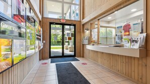 Zona de recepción con detalles de madera, puerta de vidrio y mostrador con folletos informativos.