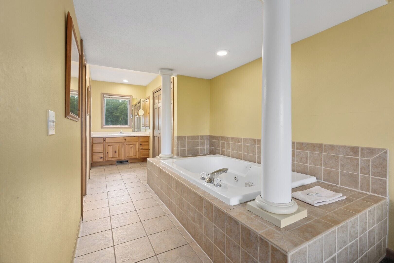 A bathroom with a large bathtub, wooden cabinets, and a tiled floor.