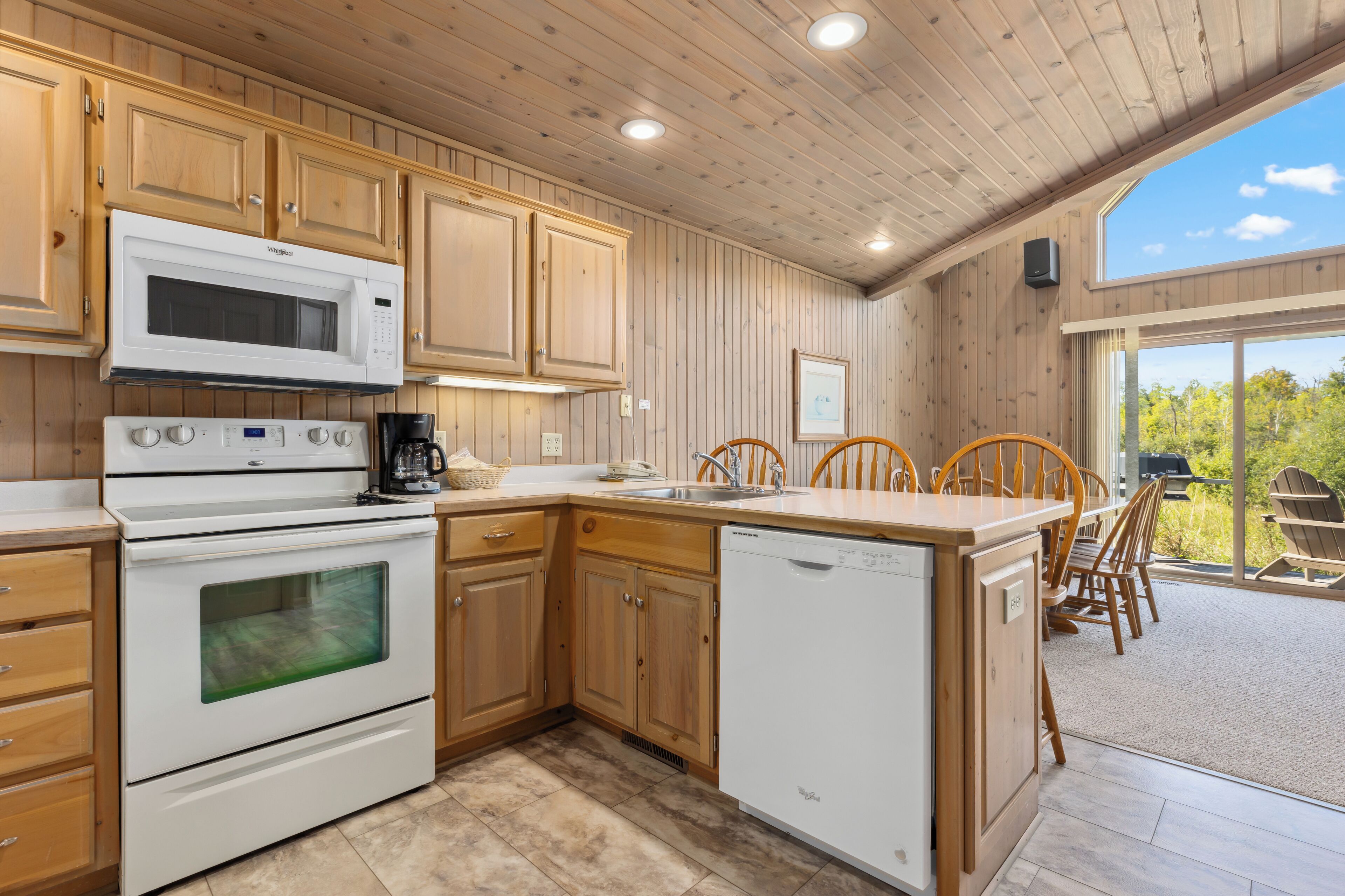 A kitchen with wooden cabinets, a microwave, an oven, and a dishwasher. There is a dining area with wooden chairs and a table.