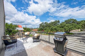 A balcony with outdoor furniture, a grill, and a view of trees and buildings. - Conveniently located | Upstairs Deck BBQ (Austin)