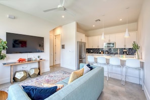 A modern kitchen with white cabinets, a stainless steel refrigerator, and a dining area with white chairs. - Conveniently located | Upstairs Deck BBQ (Austin)