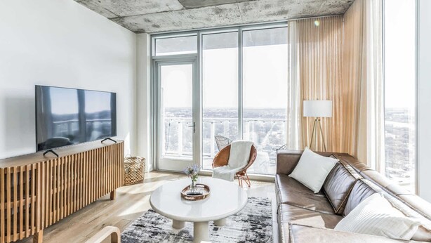Een moderne woonkamer met een grote televisie, een bank, een salontafel en uitzicht op de stad door grote ramen.
