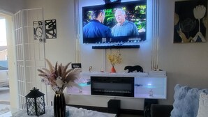 Een moderne woonkamer met een flatscreen televisie aan de muur, een witte salontafel, een zwarte bank en decoratieve items, waaronder een vaas en een zwarte lantaarn.