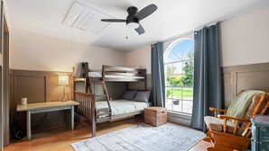 Une chambre avec un lit superposé, un bureau, une chaise, un radiateur et une fenêtre avec des rideaux.