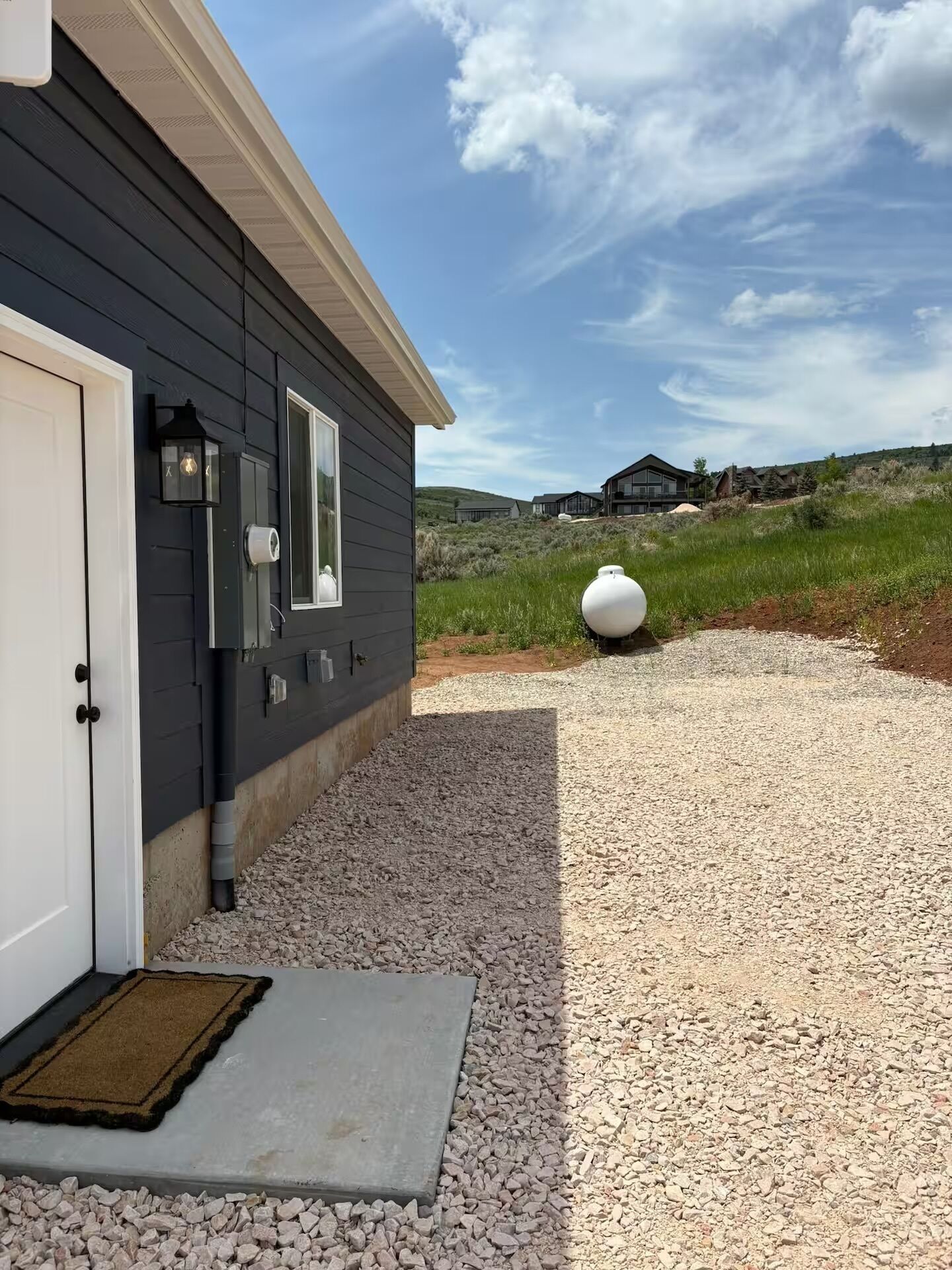 A house with a gravel driveway, a doormat, and a large decorative sphere.