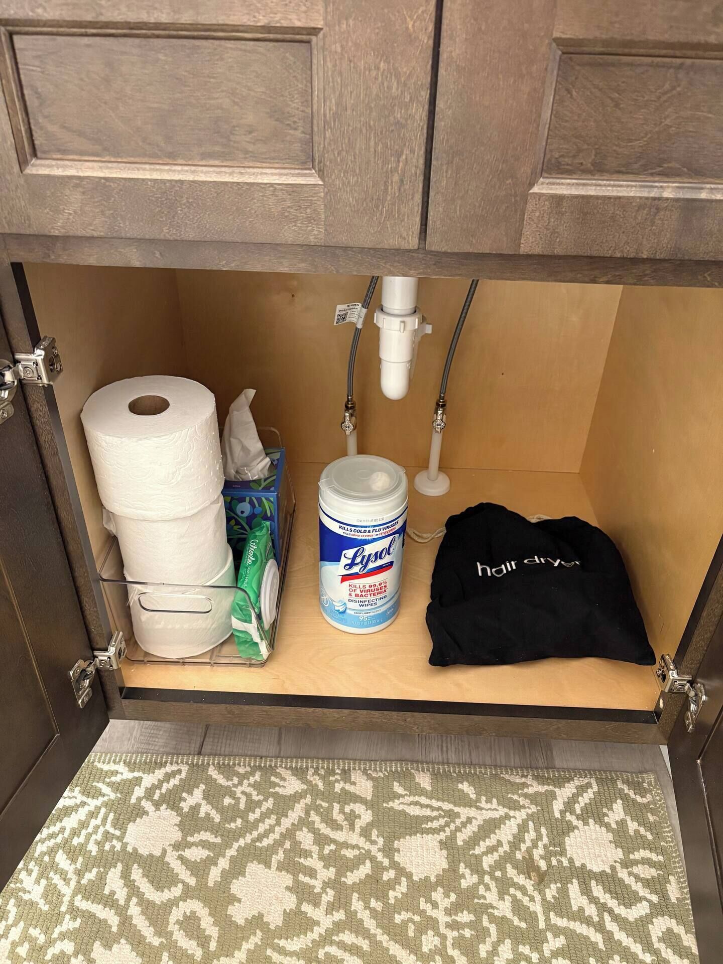 Ein Badezimmer mit Toilettenpapierrolle, Lysol-Feuchttüchern, einem Haartrockner und einer schwarzen Tasche.