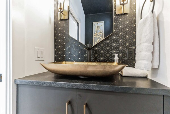 A bathroom with a vessel sink, a mirror, a towel, and a geometric-patterned wall.