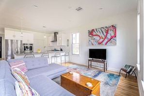 A modern living room with a grey sofa, a wooden coffee table, a colorful rug, a TV, and a kitchen in the background. - Rooftop Deck | 2 Miles to Downtown (Austin)