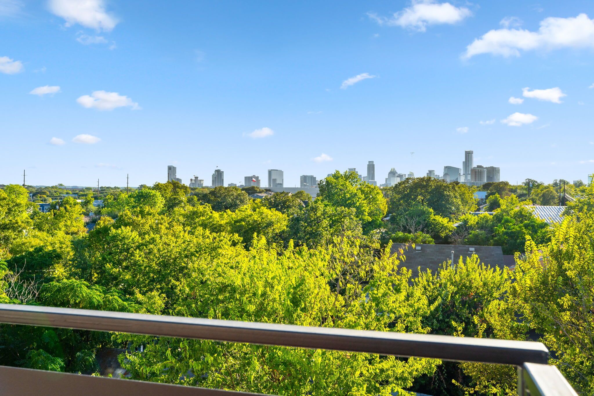 A city skyline with modern buildings, lush green trees, and a clear blue sky.
