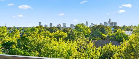 A city skyline with modern buildings, lush green trees, and a clear blue sky.