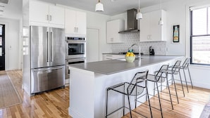 A modern kitchen with stainless steel appliances, a central island with bar stools, and a window providing natural light. - 3BR w/ Rooftop Deck, Near DT, Sleeps 6! (Austin)