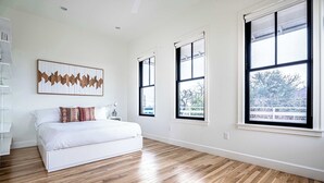 A bedroom with a bed, a bedside table, a lamp, and a large window. - 3BR w/ Rooftop Deck, Near DT, Sleeps 6! (Austin)