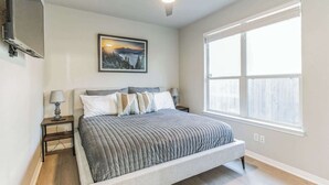 A bedroom with a bed, a nightstand, a ceiling fan, a window, and a painting on the wall. - South Austin 2BR | Close to SoCo/Zilker | Sleeps 4 (Austin)