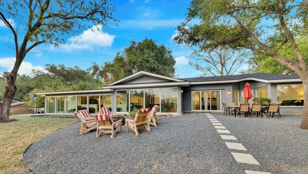 Una casa moderna con un patio, mobiliario exterior y un camino de entrada de grava.
