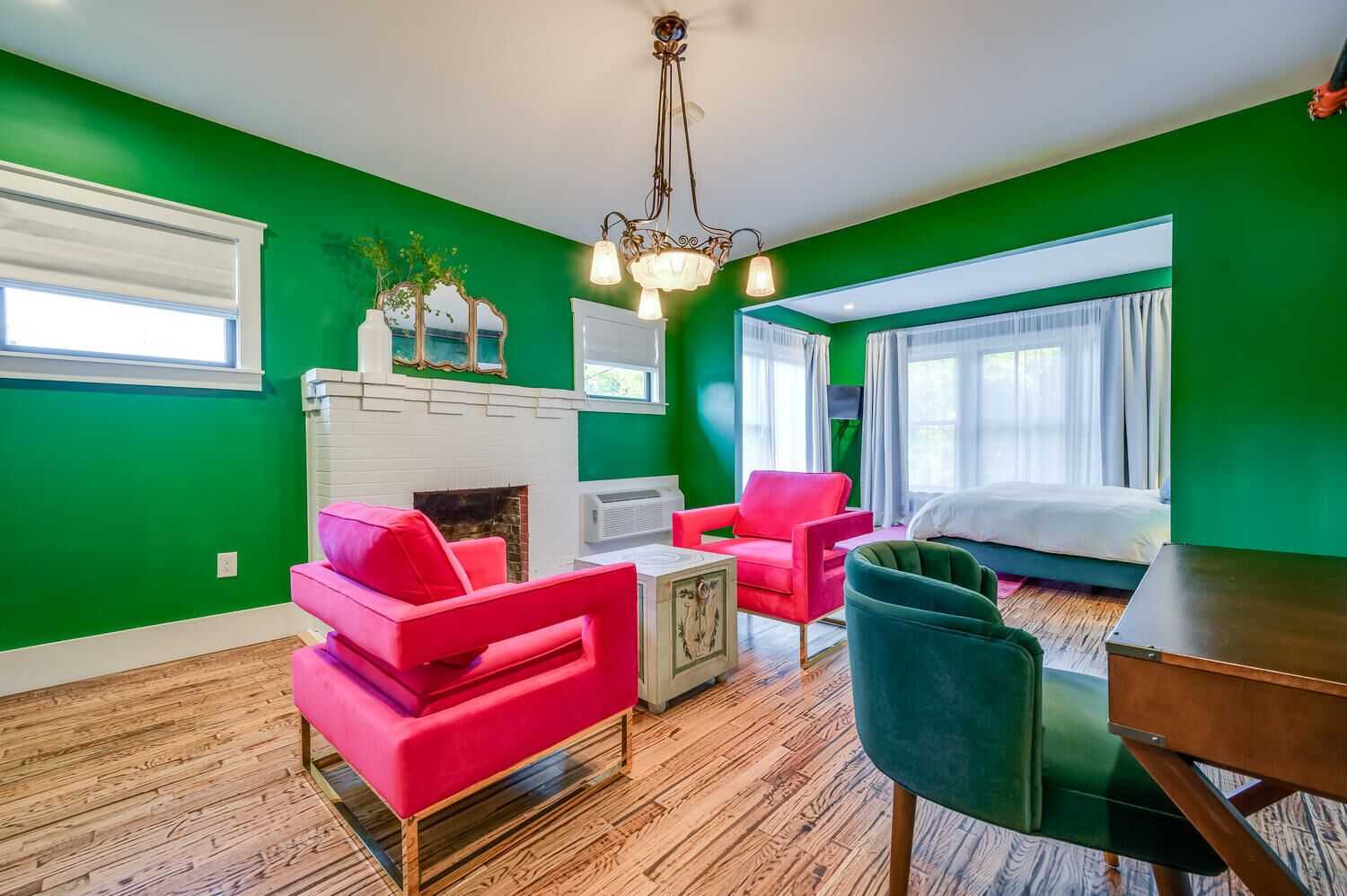 Une pièce aux murs verts, avec une cheminée blanche, un lit, une table à manger et deux chaises.