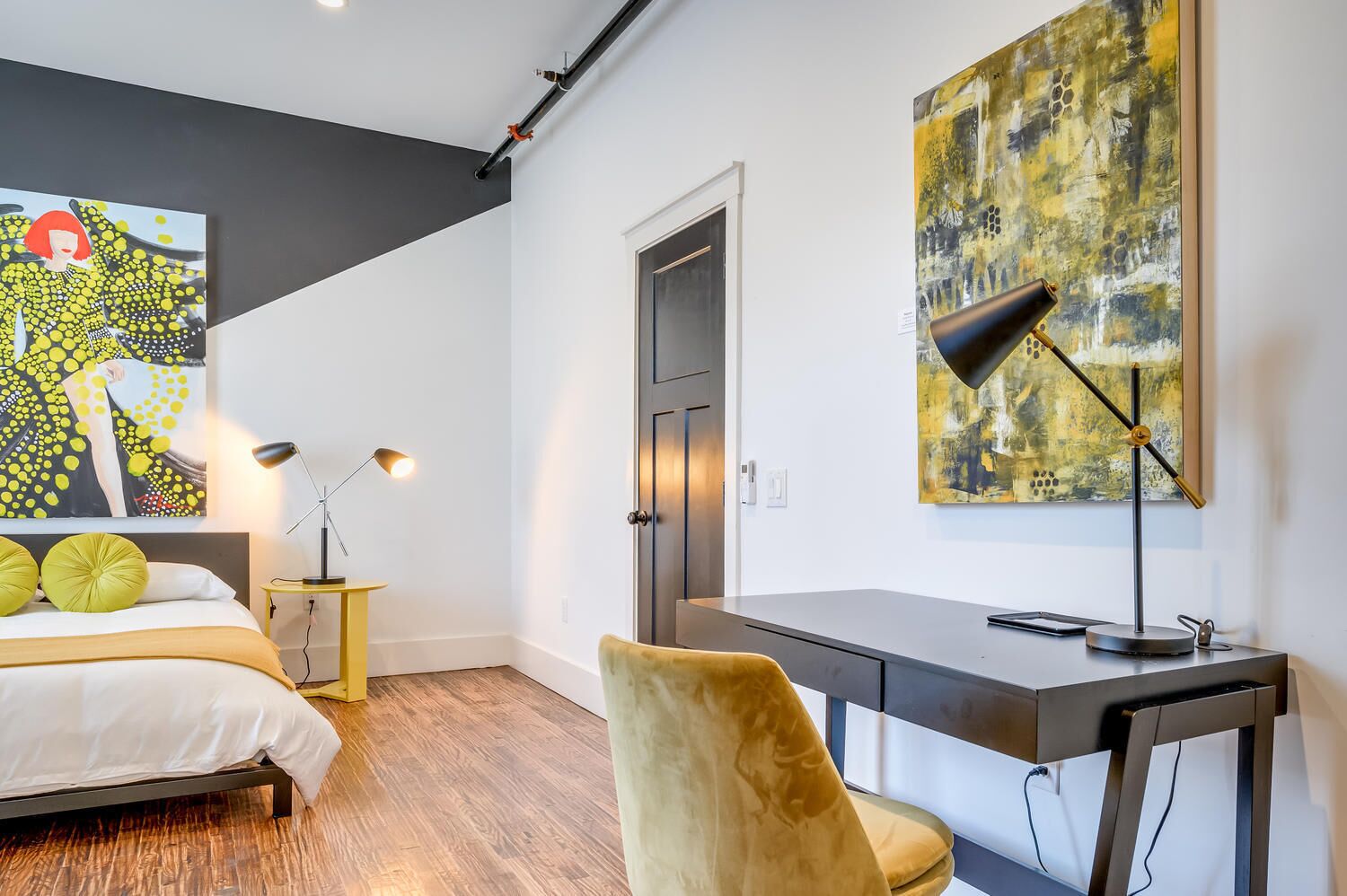 Une chambre moderne avec un lit, un bureau, une chaise et des œuvres d’art.