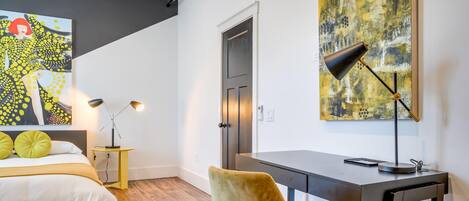 A modern bedroom with a bed, desk, chair, and artwork.