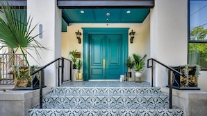 A teal door with a patterned tile entrance, potted plants, and a mailbox.