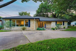 A single-story stone house with a dark roof, a front porch, and a small front yard.