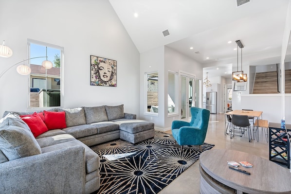 A modern living room with a sectional sofa, a blue armchair, and a dining area with a table and chairs.
